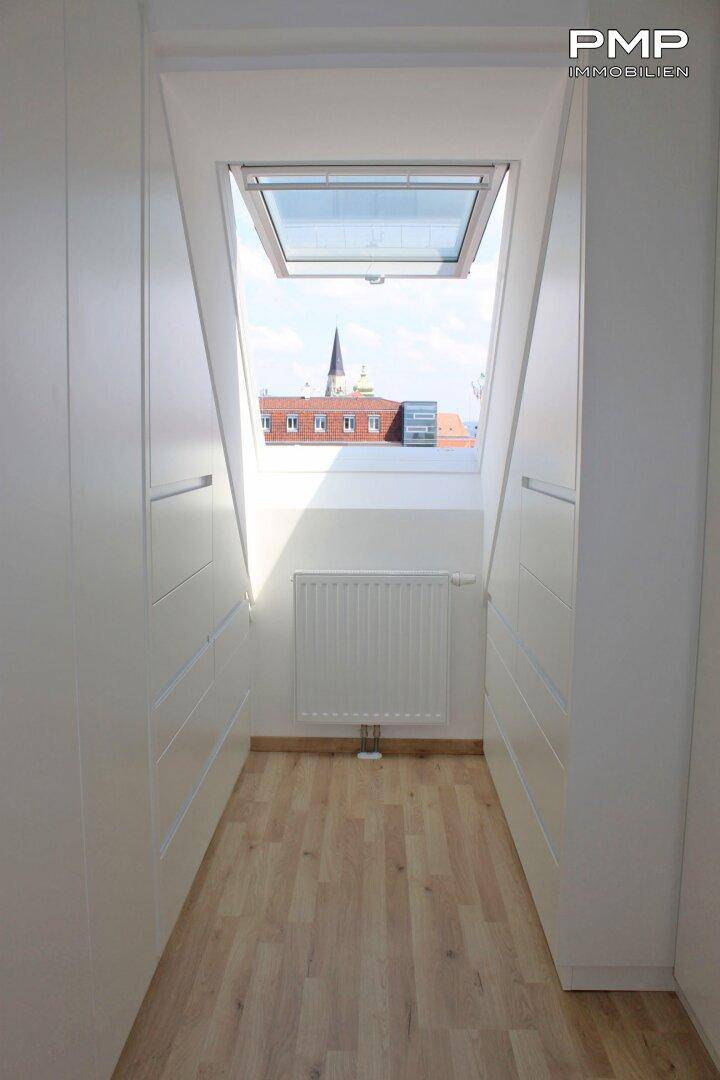 Heller Flur mit Einbauschränken, Dachfenster und Blick auf die Dächer der Stadt.