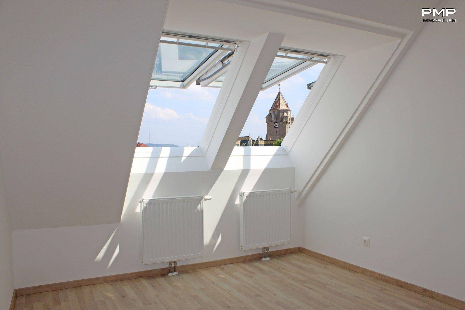 Helles Dachzimmer mit zwei großen Dachfenstern und Blick auf den Kirchturm.