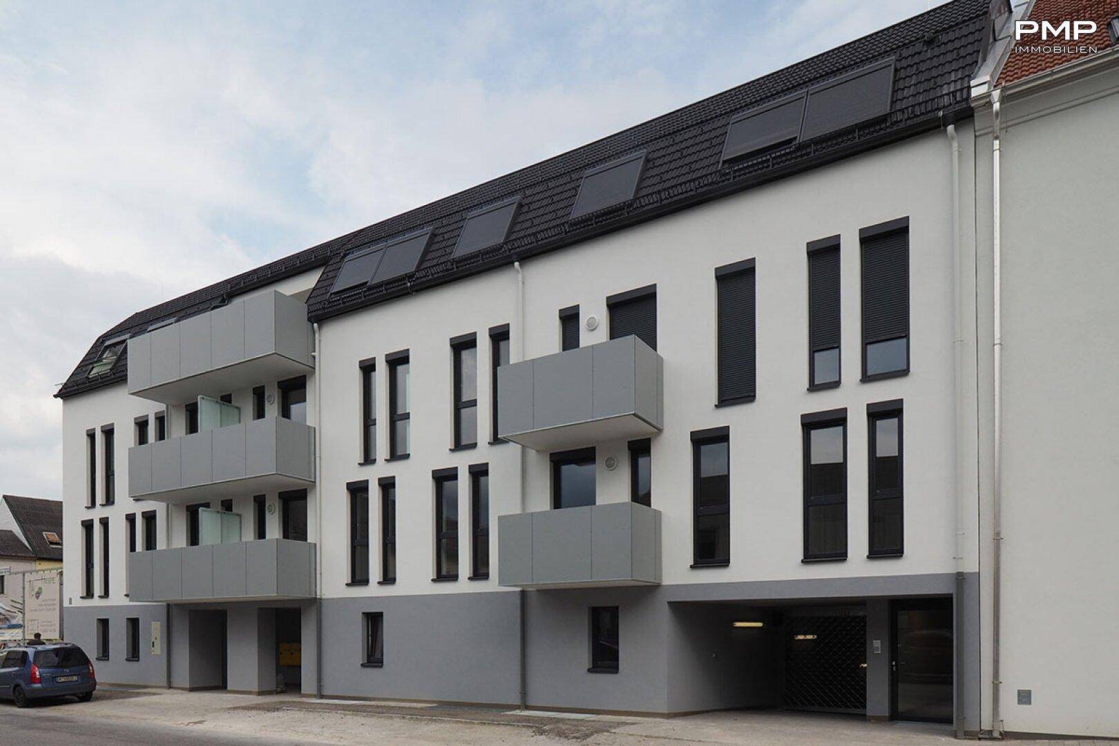 Moderne Wohnanlage mit weißer Fassade, grauen Balkonen und Dachfenstern.