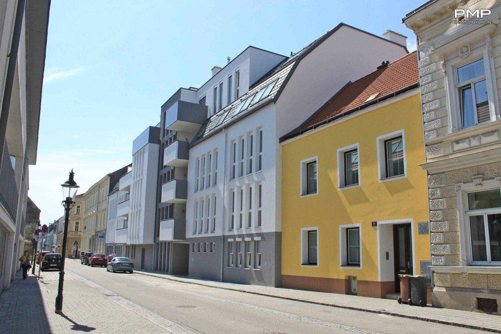 Moderne und traditionelle Gebäude entlang einer ruhigen Stadtstraße unter blauem Himmel.