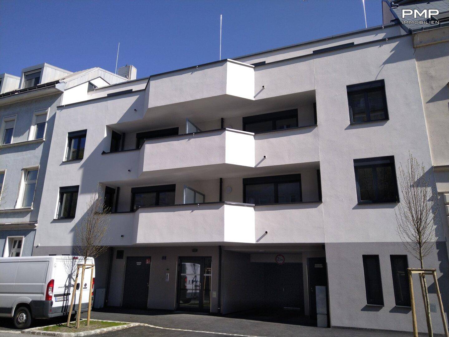 Neubau-Wohngebäude mit moderner Architektur, weißen Balkonen und ebenerdigen Zugängen.