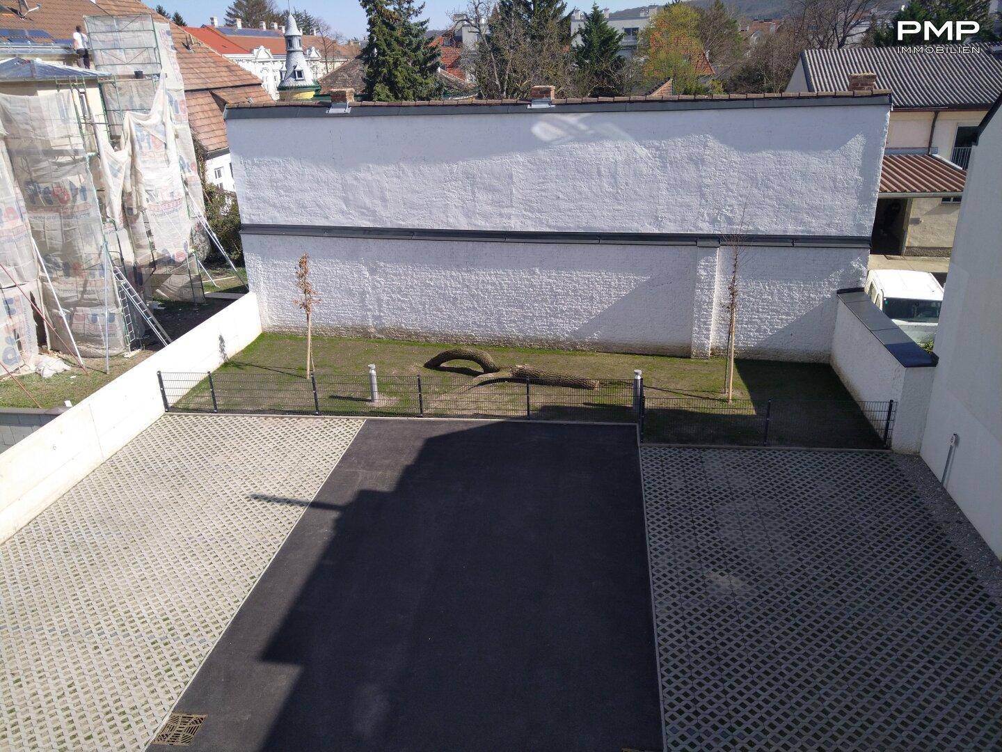 Blick von oben auf die Außenanlage mit Parkplätzen, Grünfläche und angrenzender Gebäudewand.