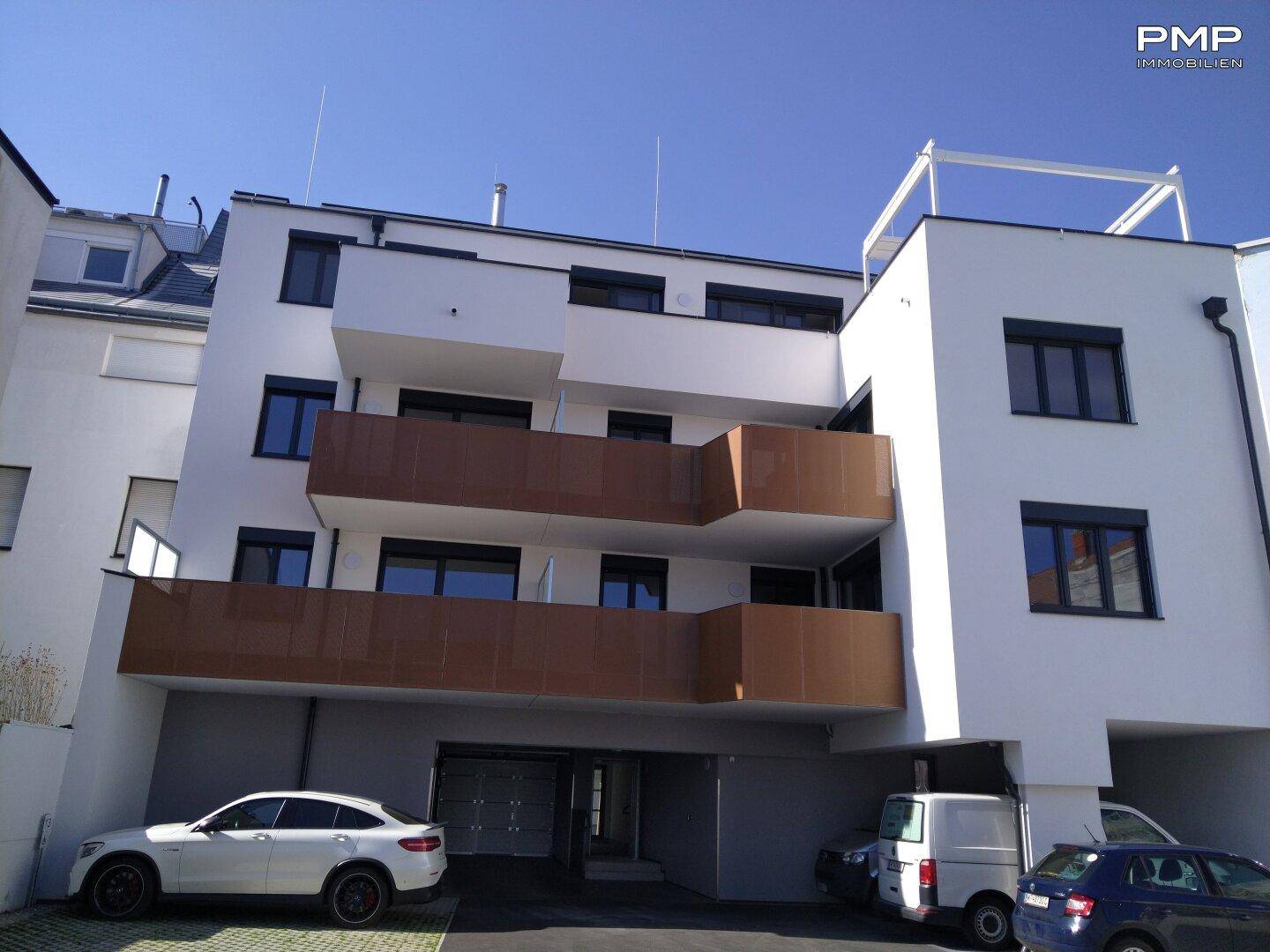 Moderne Wohnhausfassade mit braunen Balkonen, großen Fenstern und Tiefgaragenzufahrt.