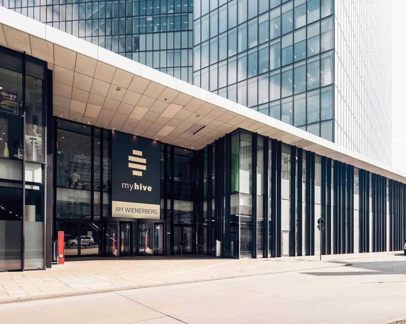 Eingangsbereich eines modernen Bürogebäudes mit großer Glasfront und schützendem Vordach.