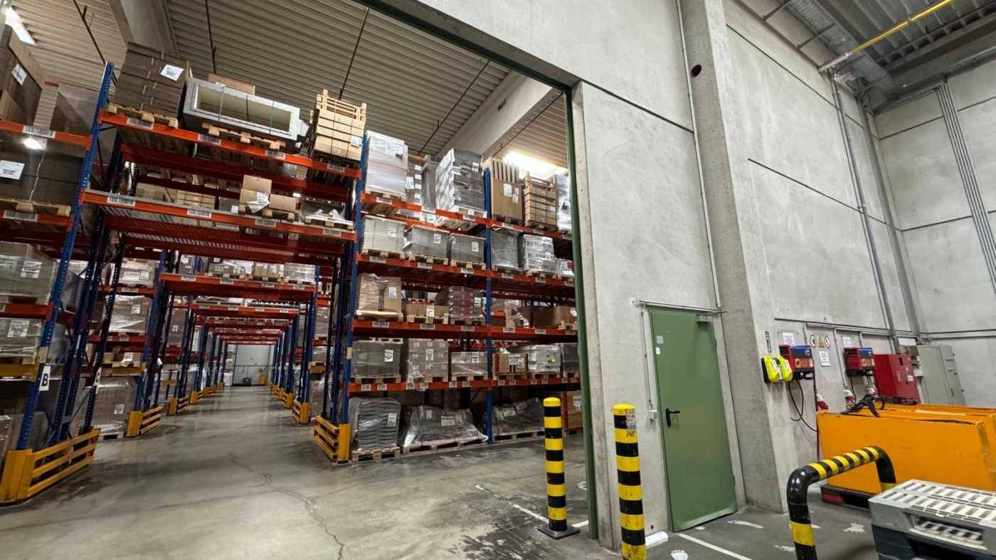 Industrieller Lagerbereich mit hohen Regalen, Betonwänden und einer grünen Zugangstür, bereit für den Betrieb.