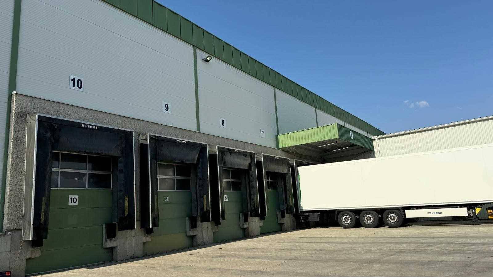 Nahaufnahme der Laderampen eines modernen Lagergebäudes mit einem parkenden LKW und klarem Himmel.
