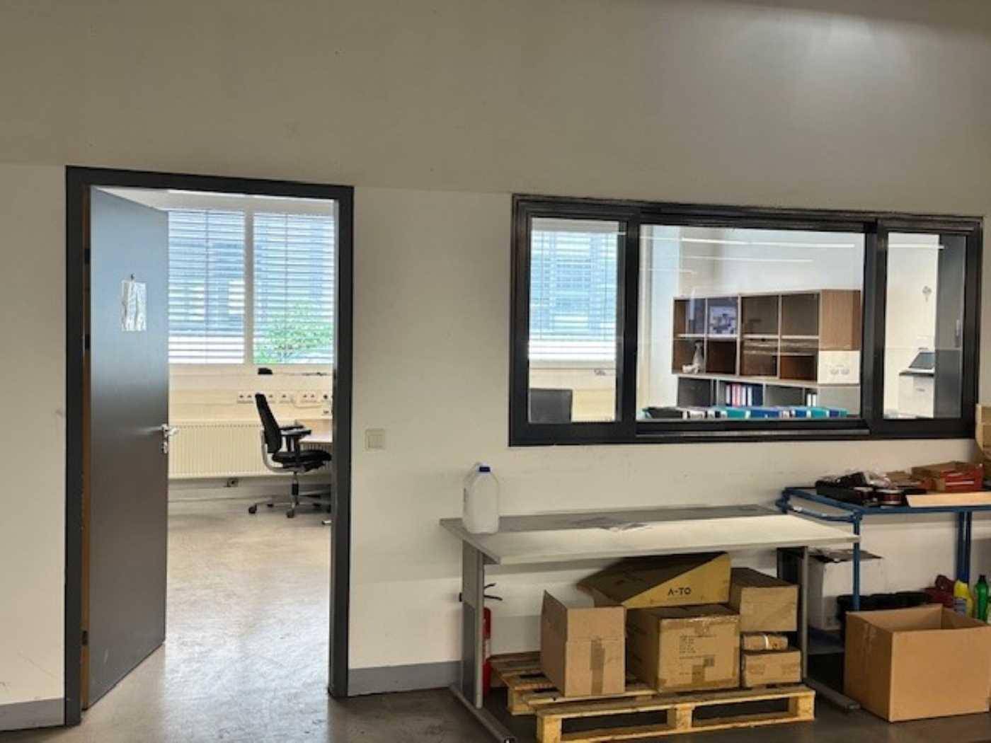 Blick in ein Büro mit Schreibtisch und Stuhl durch eine offene Tür und ein Fenster.