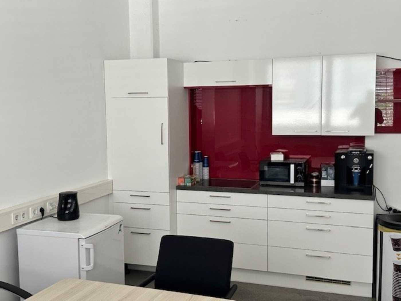 Kleine, moderne Küchenzeile mit weißen Schränken, roter Rückwand und grundlegenden Geräten.