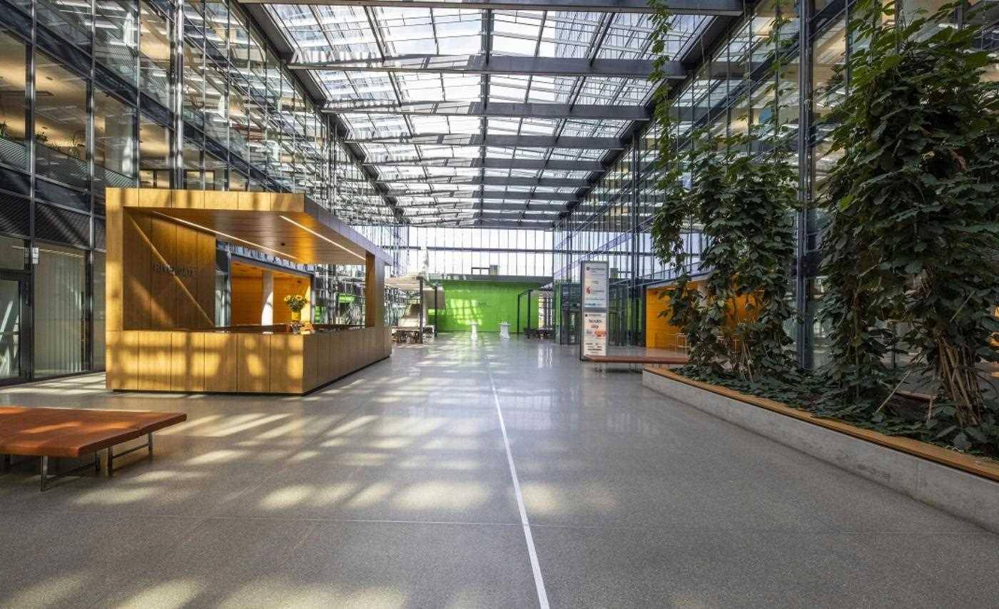 Helle, moderne Lobby mit Glasdach, Empfangsbereich und viel Grünpflanzen.