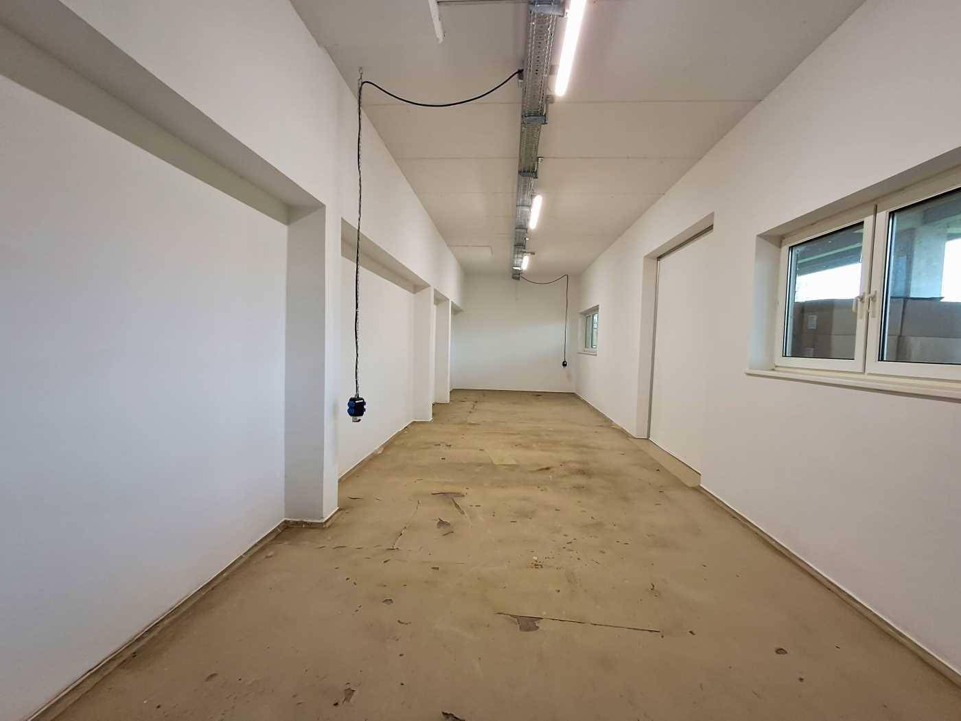 Geräumiger, heller Flur oder Arbeitsbereich mit weißen Wänden, Betonboden und sichtbaren Deckenleuchten.