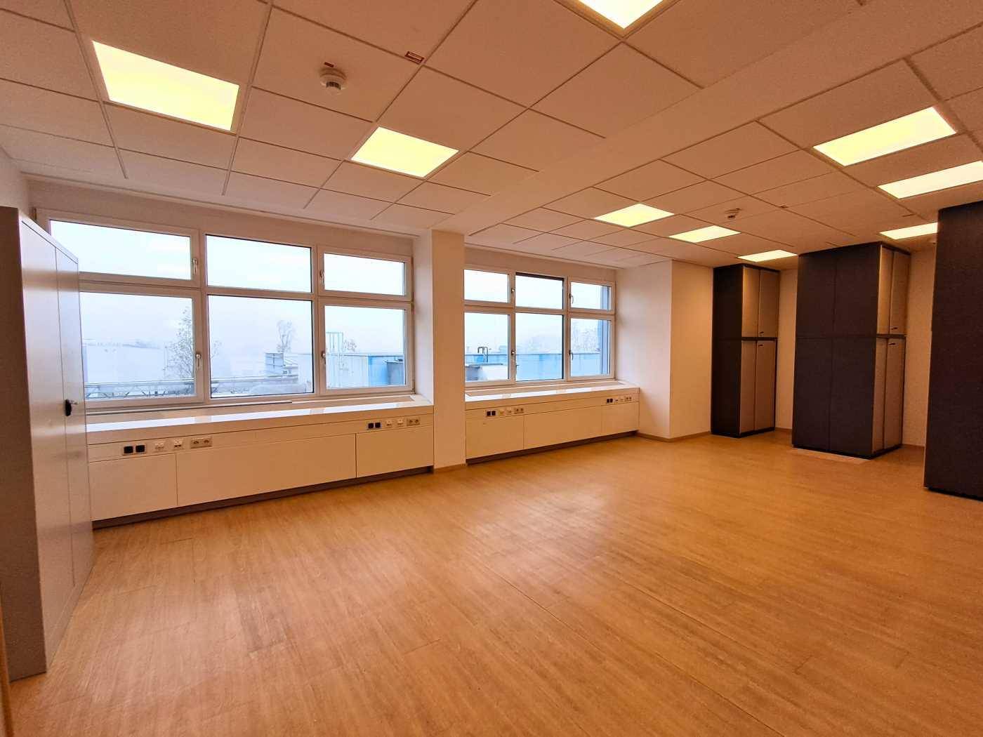 Geräumiges und helles Büro mit großen Fenstern, Einbauschränken und Holzfußboden.