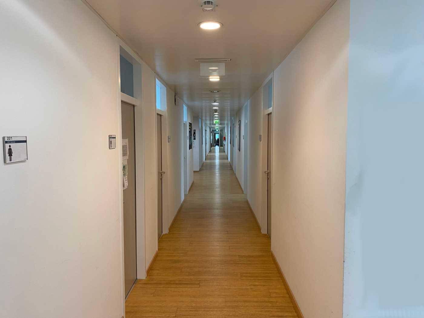 Langer, heller Flur mit Holzboden und mehreren Türen, der zu verschiedenen Räumen führt.