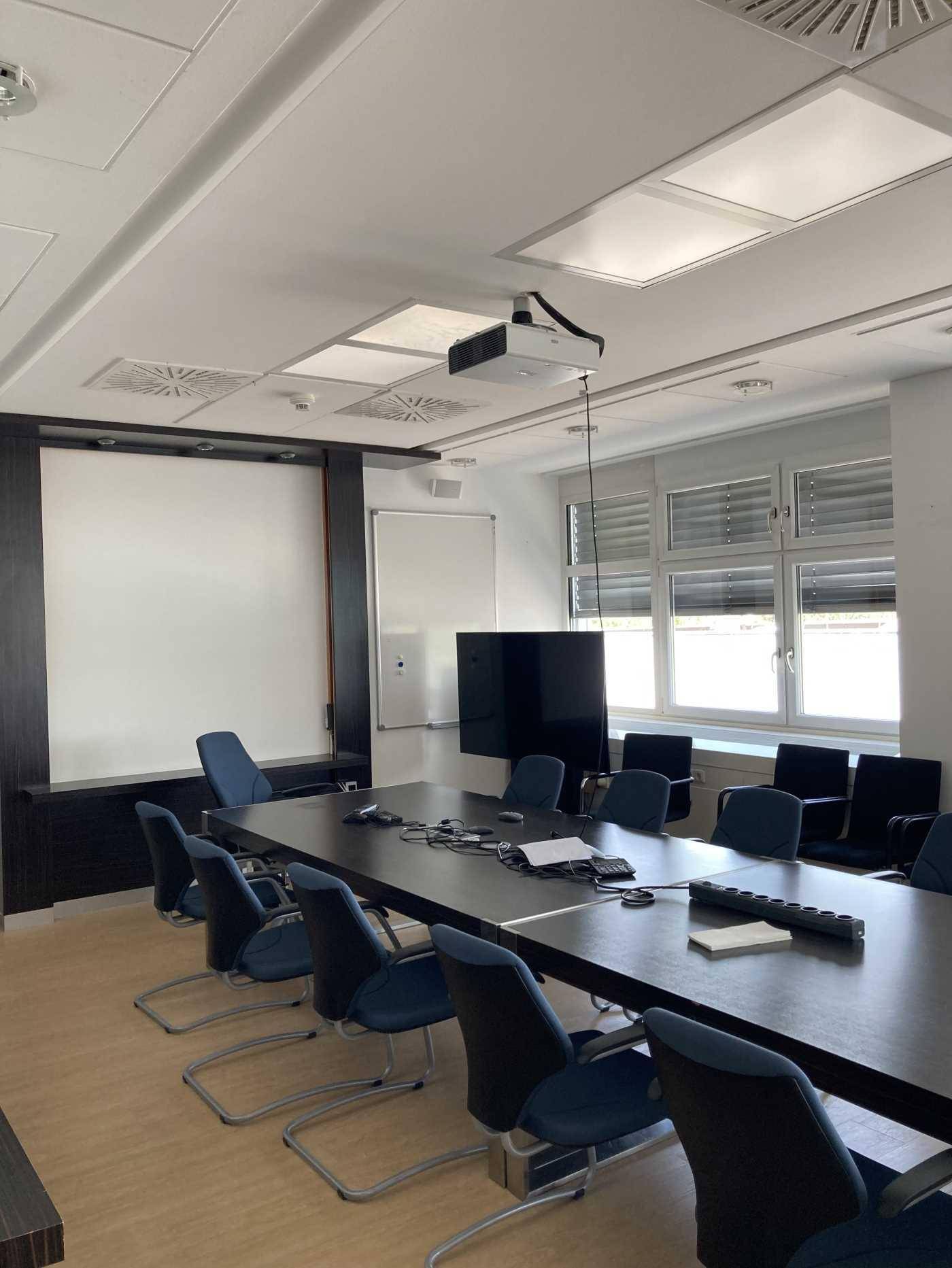 Moderner Konferenzraum mit großem Tisch, Projektor und bequemen Stühlen für Besprechungen.