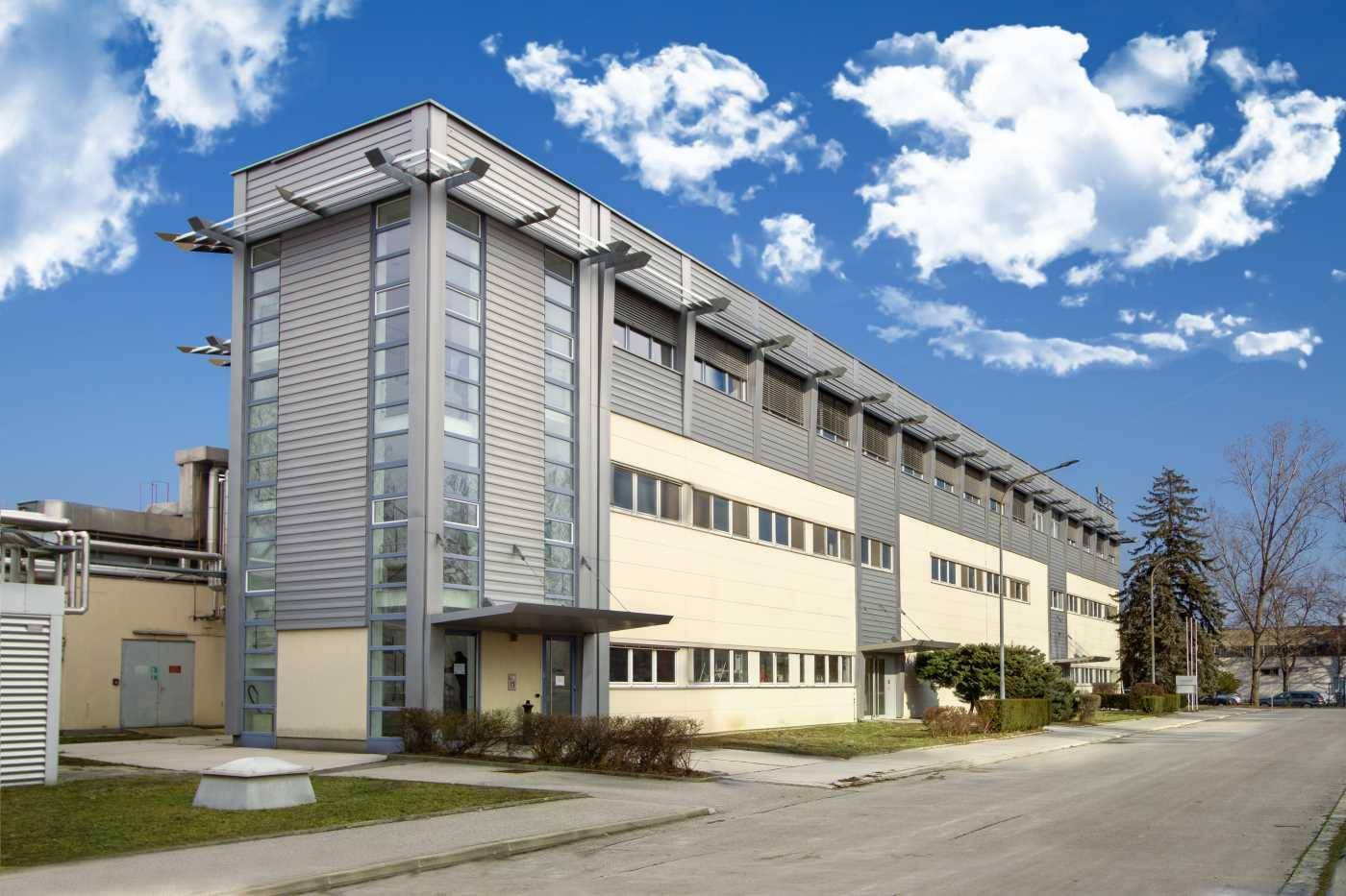 Modernes Geschäftsgebäude mit Glasfassade und Metallverkleidung unter einem blauen Himmel mit Wolken.