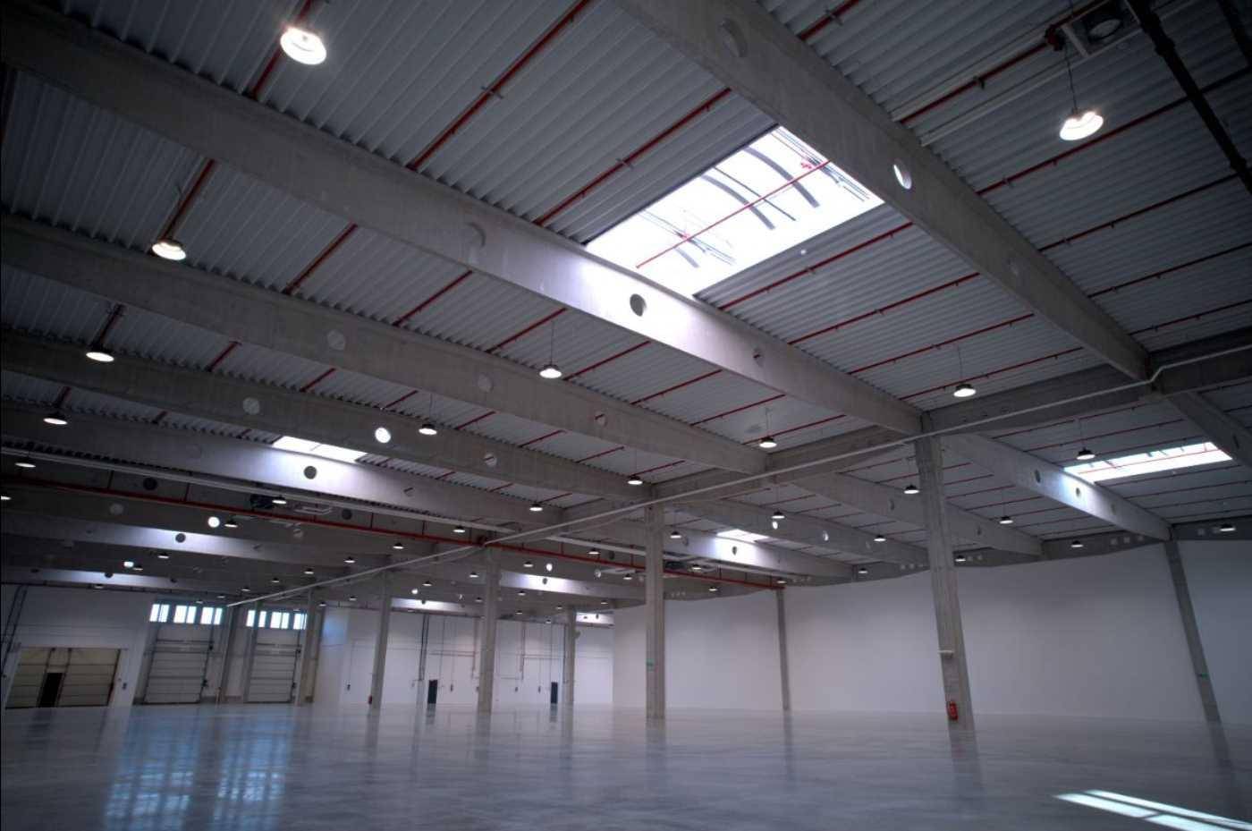 Weitläufige Lagerhalle mit hohen Decken, Oberlichtern und industrieller Beleuchtung, bereit zur Nutzung.