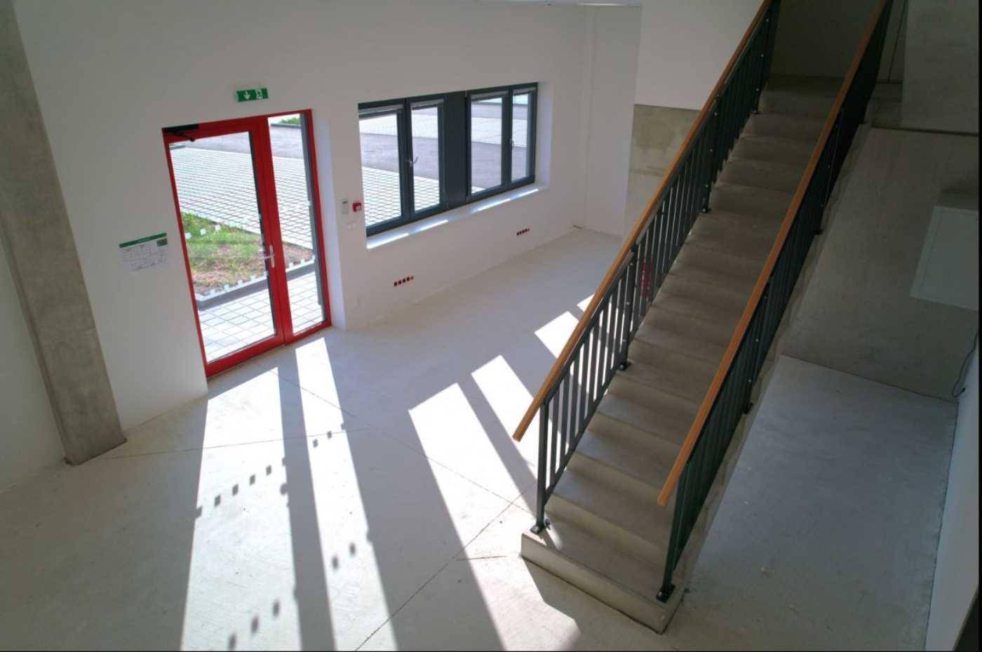 Eingangsbereich mit Treppe und roter Tür, die zu den Außenparkplätzen führt, hell beleuchtet.