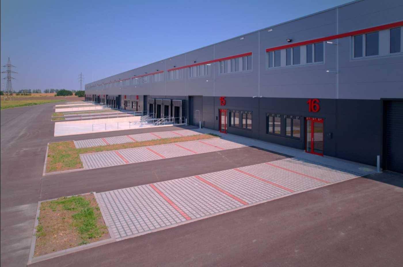 Nahaufnahme der modernen Fassade eines Lagergebäudes mit mehreren Laderampen und Parkplätzen.