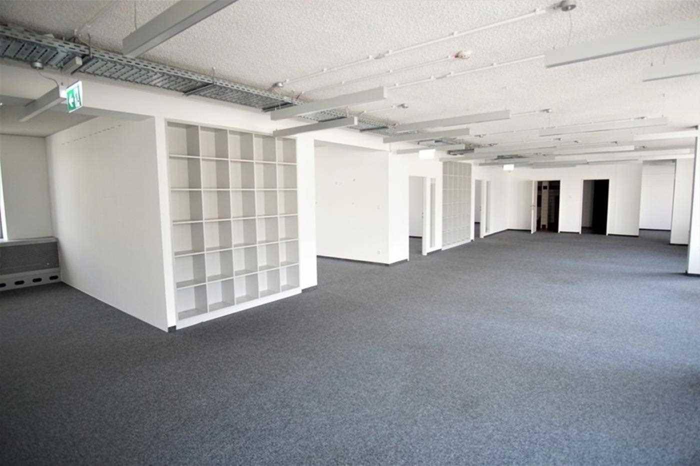 Geräumiges, leeres Büro mit grauem Teppichboden, weißen Wänden und integrierten Regalen.