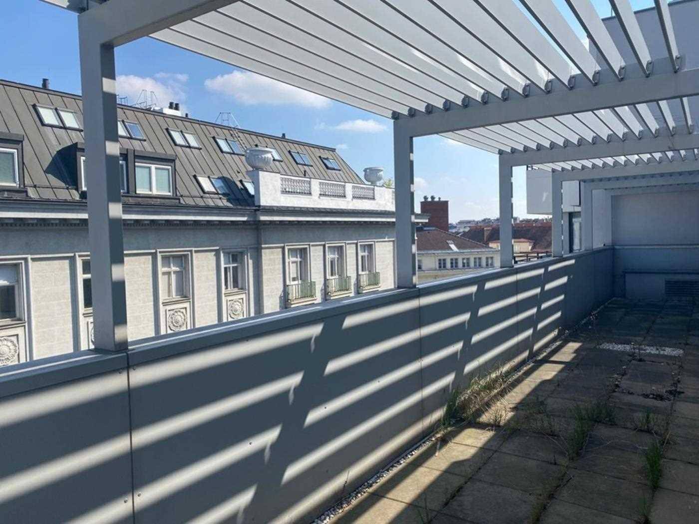 Dachterrasse mit Pergola und Blick auf umliegende Gebäude unter blauem Himmel.