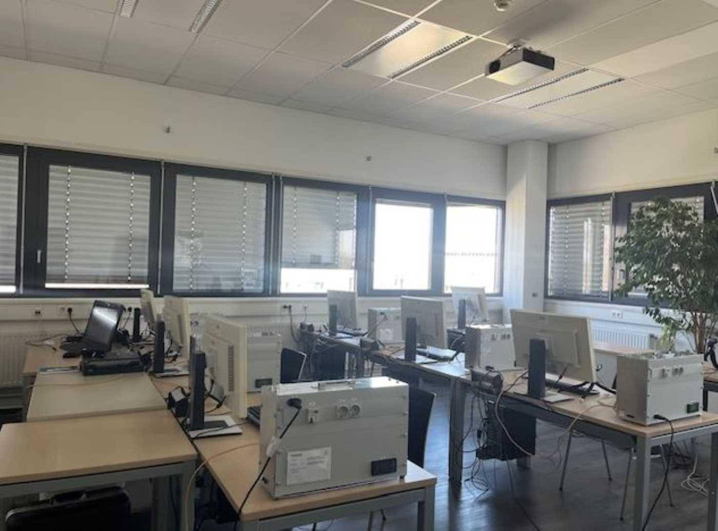 Computerraum mit mehreren Arbeitsplätzen, Monitoren und einem Projektor an der Decke.