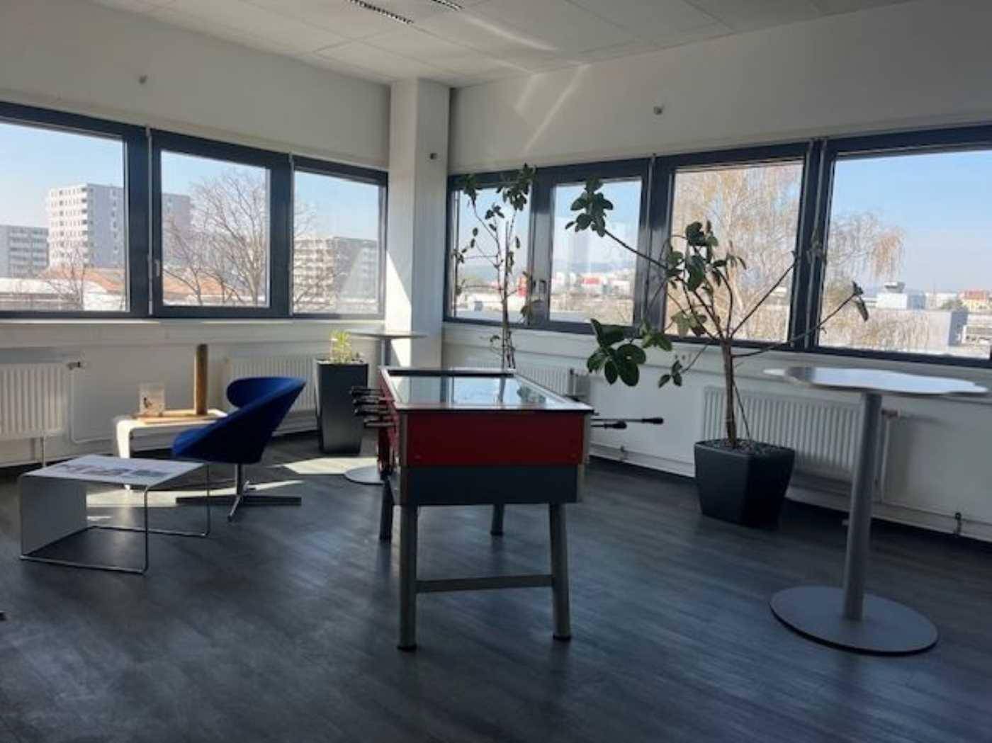 Heller Loungebereich mit einem Kicker, modernen Sitzgelegenheiten und großen Fenstern mit Stadtblick.