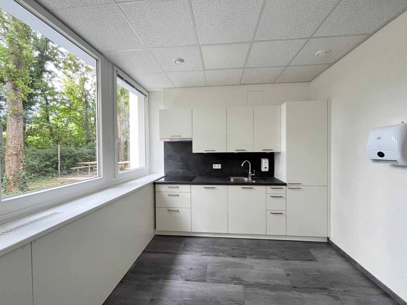 Moderne Küchenzeile mit weißen Schränken, dunkler Arbeitsplatte und großem Fenster mit Blick ins Grüne.