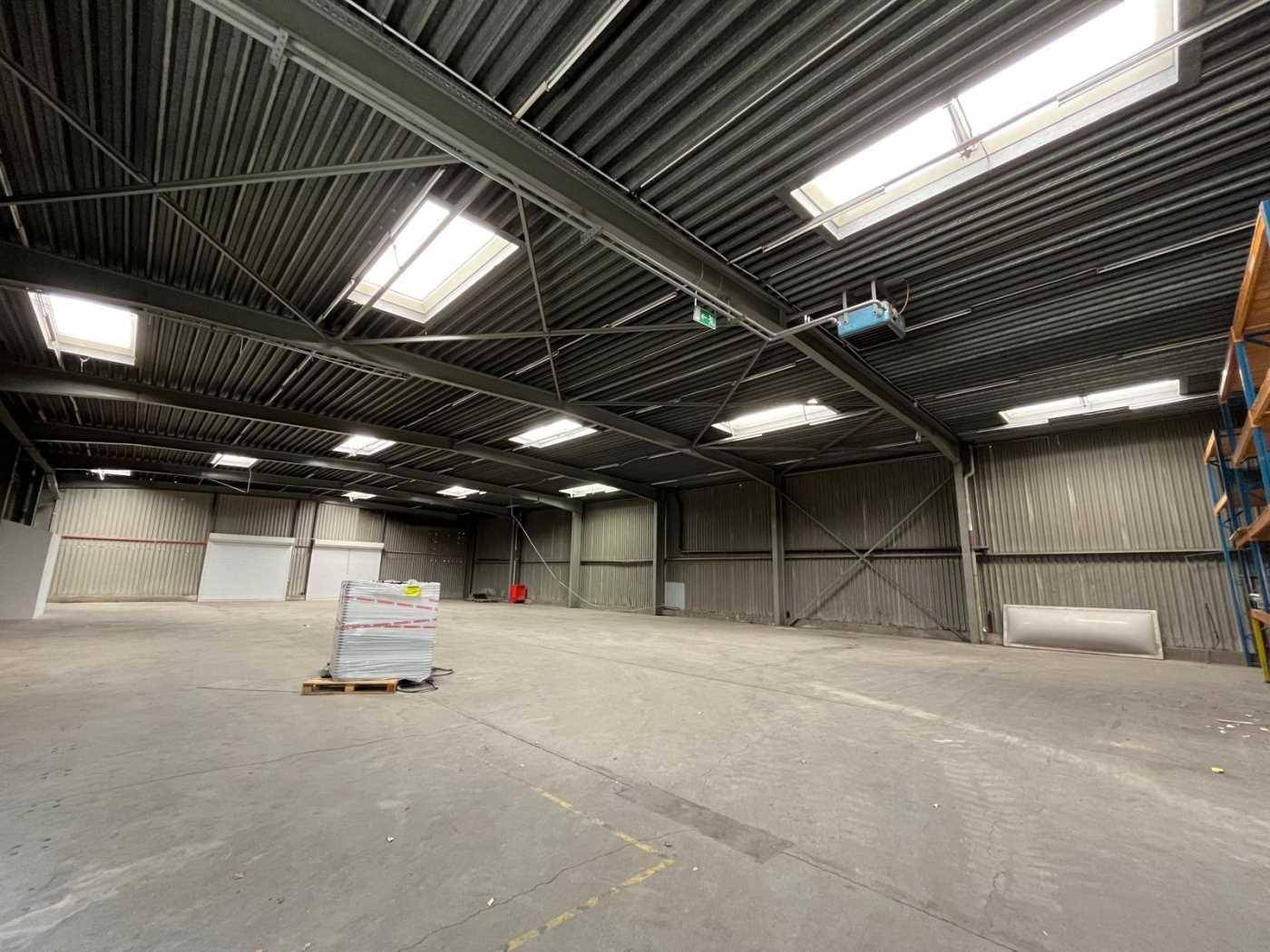 Weitläufige Lagerhalle mit hohen Decken, Oberlichtern und einem Betonboden.