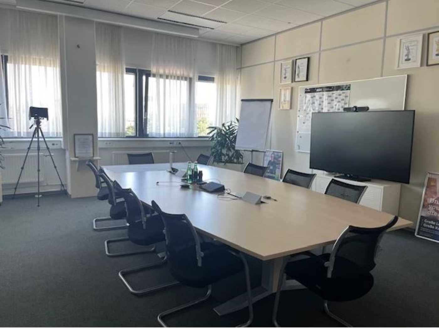 Geräumiger Konferenzraum mit großem Tisch, vielen Stühlen und einem Bildschirm für Präsentationen.