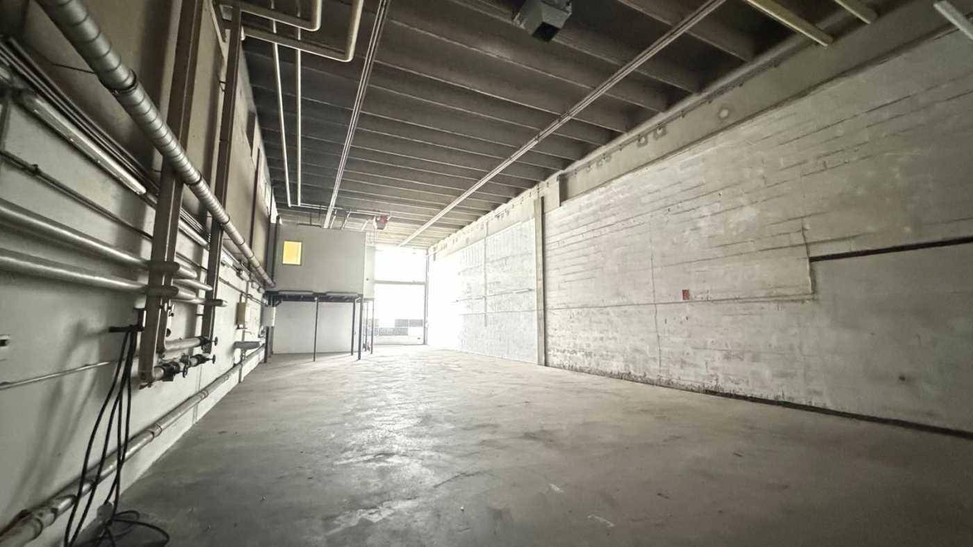 Langer, leerer Industrieraum mit Betonboden, sichtbaren Rohren und einer hohen Decke, der vielseitig nutzbar ist.