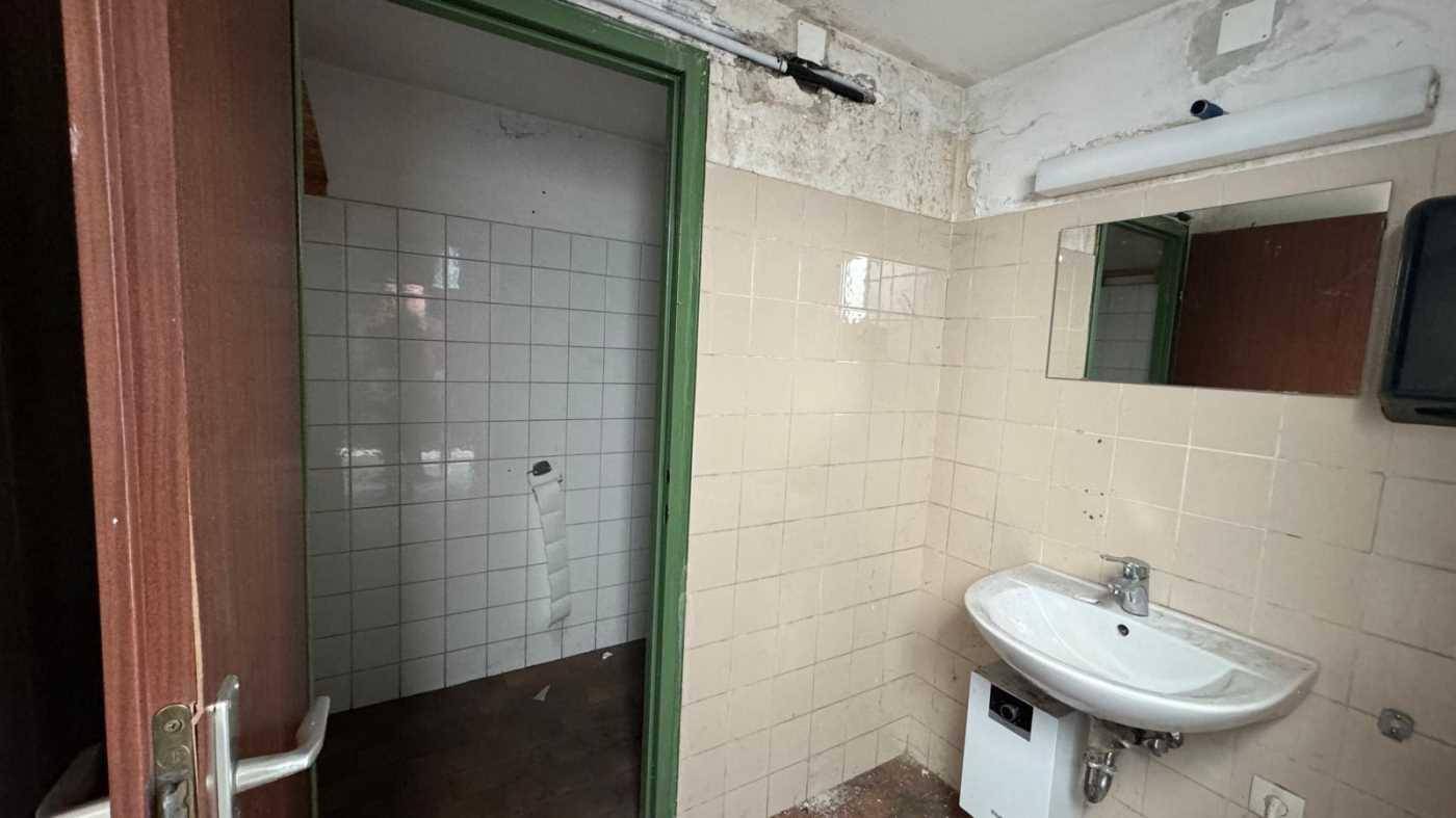 Einfaches Badezimmer mit Waschbecken, Spiegel und gefliesten Wänden, das Renovierungsbedarf zeigt.