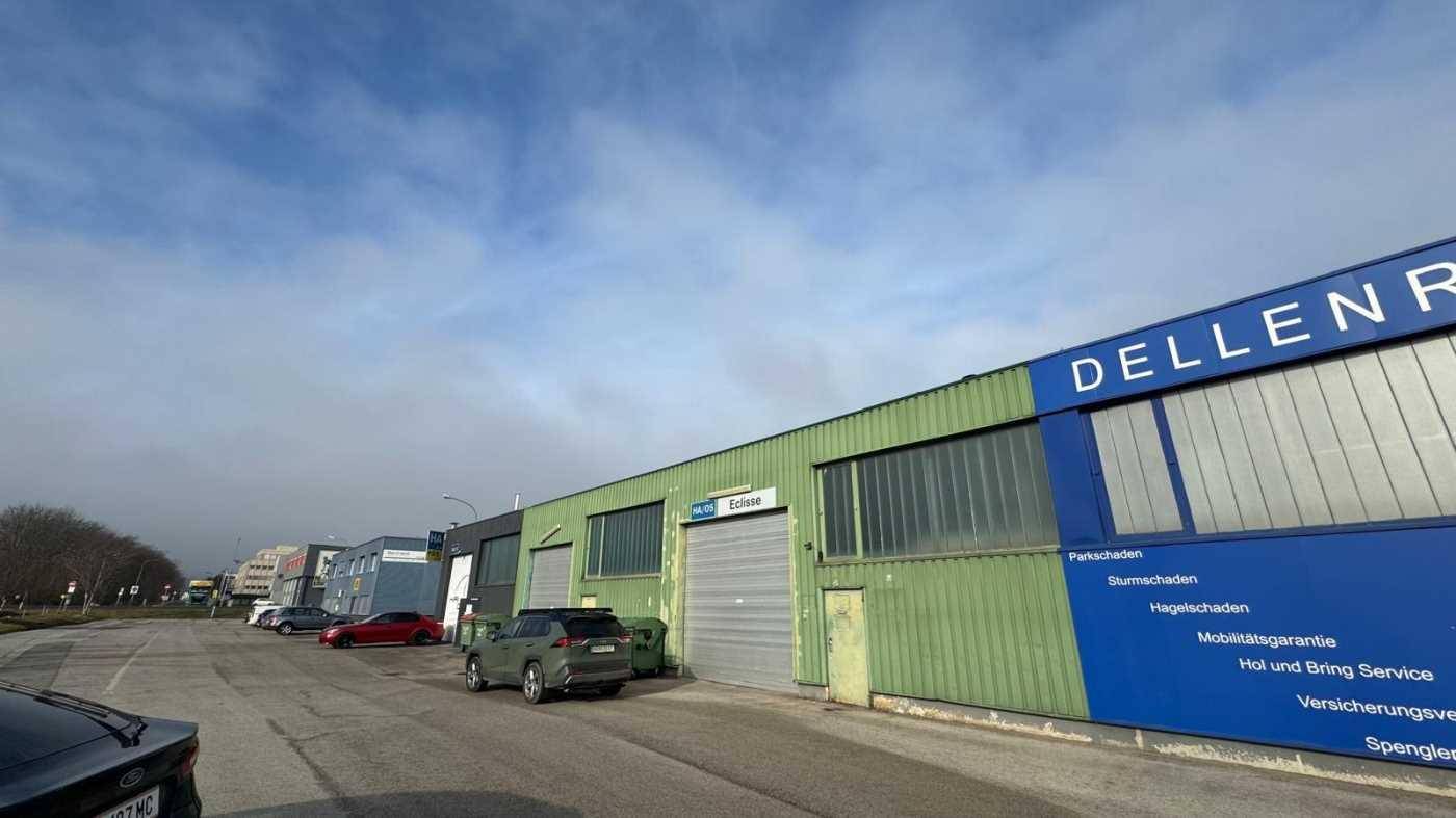 Grüne Industriefassade mit großen Rolltoren und Beschilderung eines Dellenreparaturdienstes, davor parken mehrere Autos.