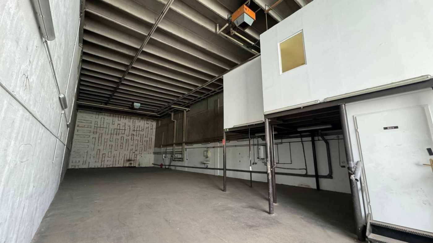 Großer Industrieraum mit Betonboden, sichtbaren Rohren und einer erhöhten Büro- oder Lagerfläche.
