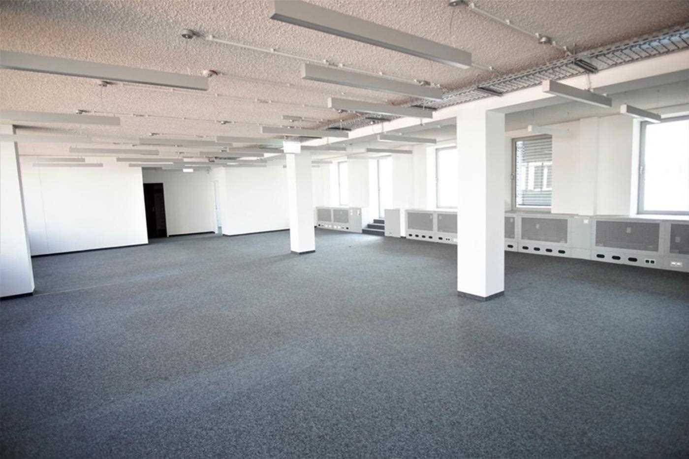 Heller Büroraum mit Säulen, großen Fenstern und grauem Teppichboden, bereit zur individuellen Gestaltung.