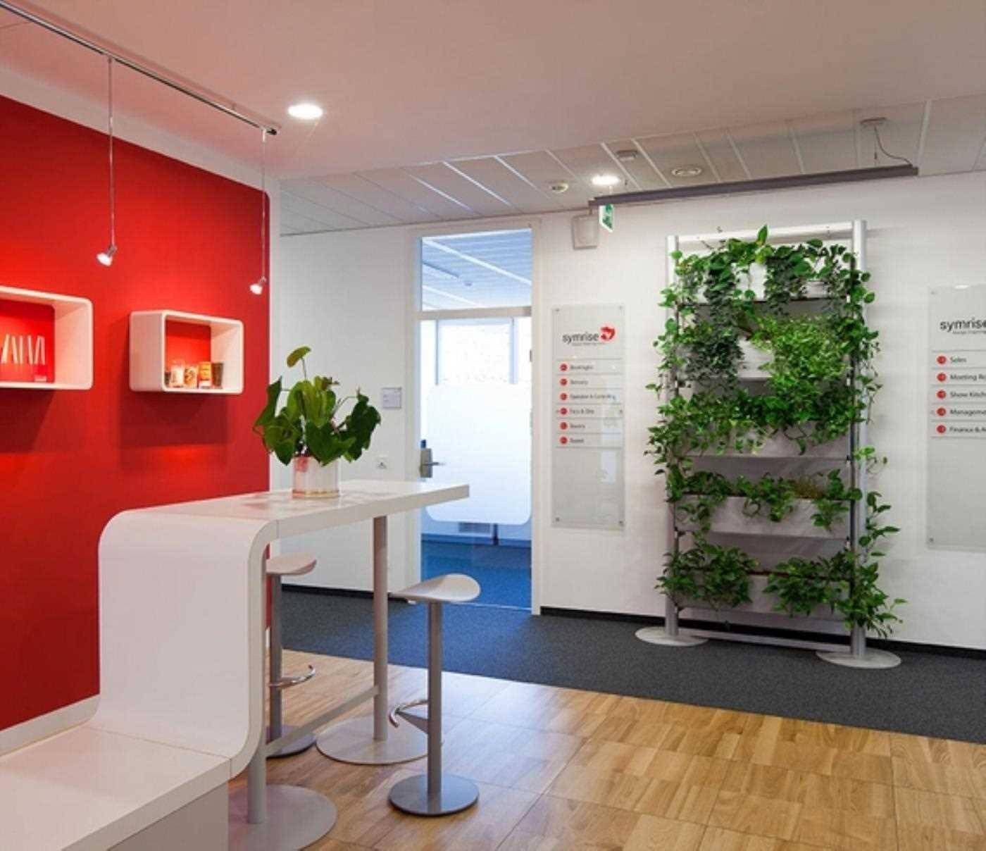 Empfangsbereich mit roter Akzentwand, Holzboden, Stehtisch und einer vertikalen Pflanzenwand für frisches Grün.