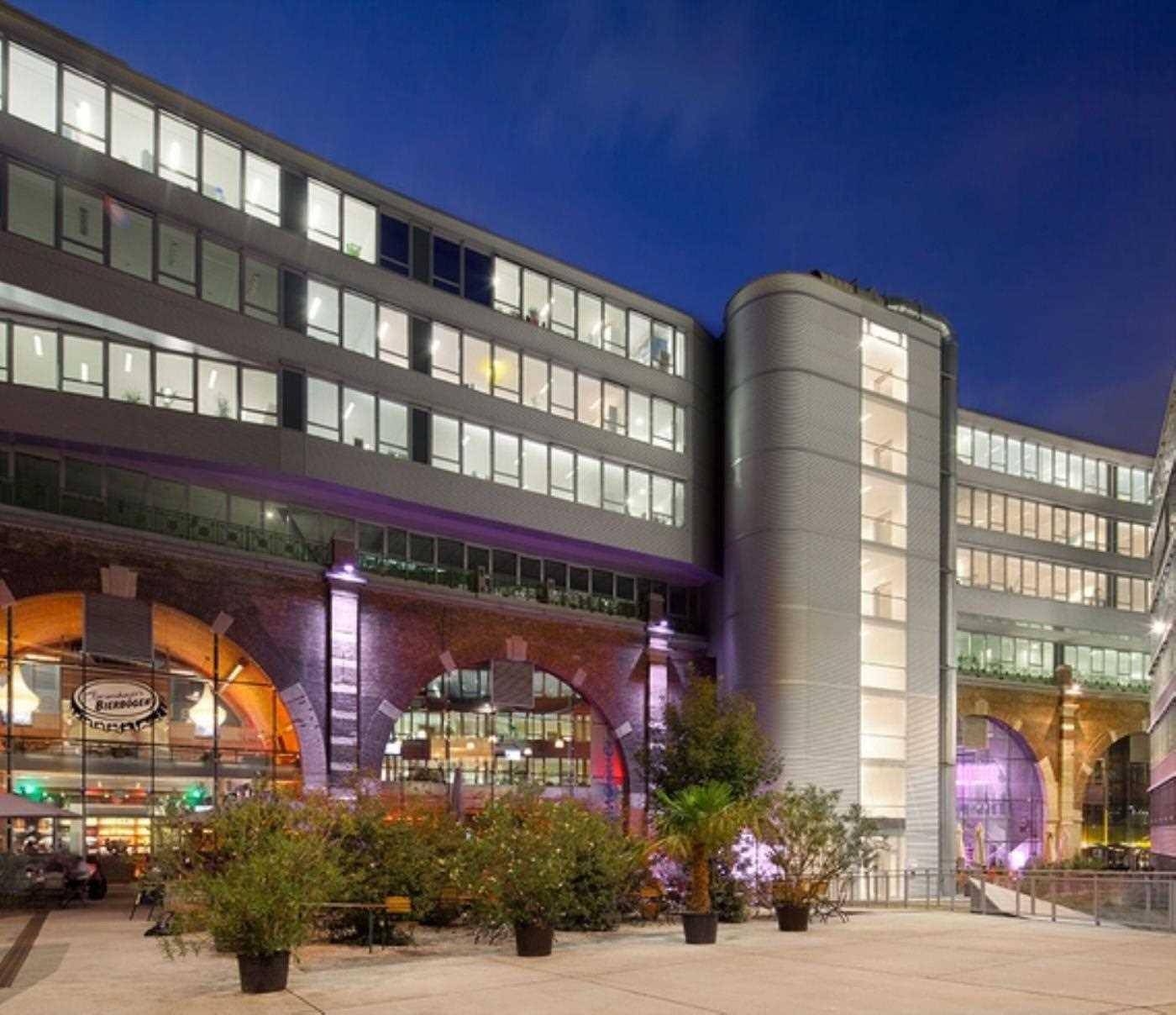 Beleuchtetes Bürogebäude bei Nacht, kombiniert moderne Architektur mit historischen Backsteinbögen und Außenbereich.