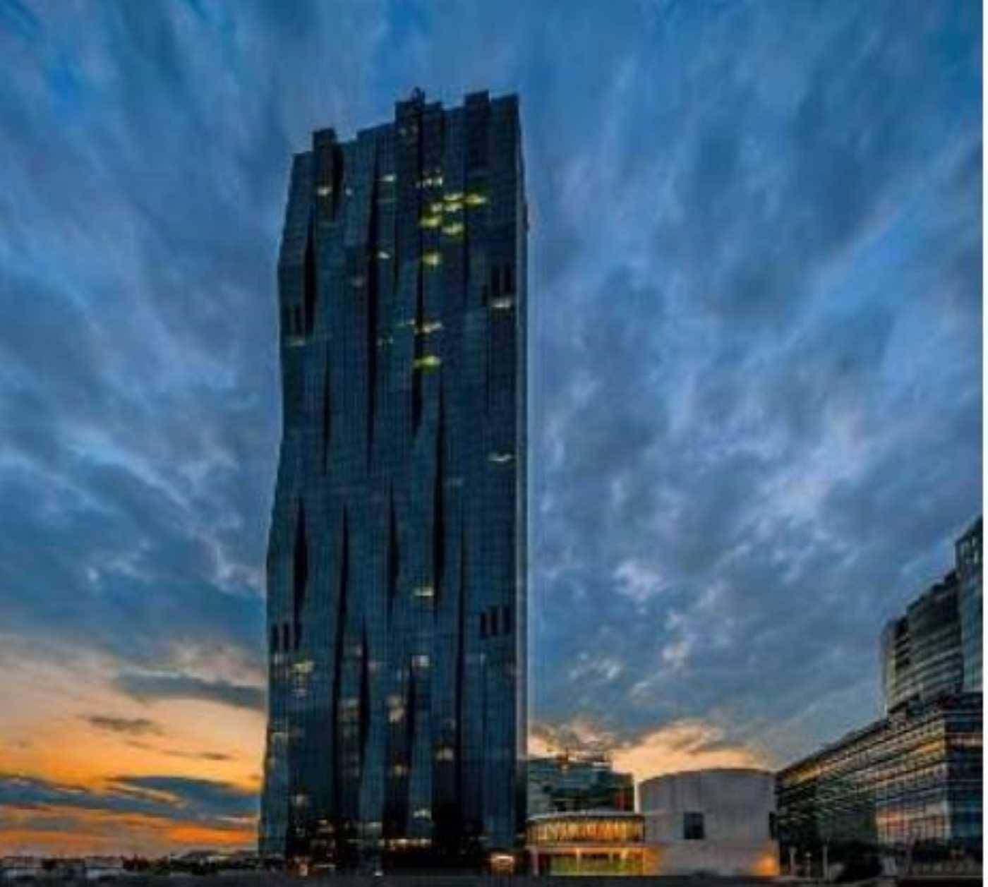 Markantes Hochhaus mit dunkler Glasfassade bei Sonnenuntergang, beleuchtet unter dramatischem Himmel.