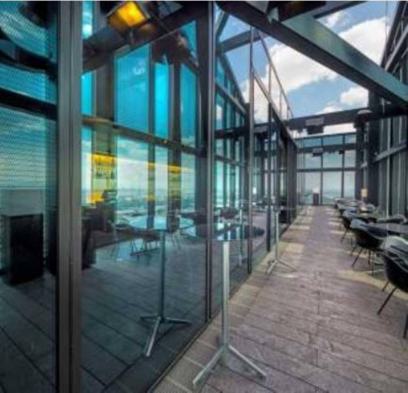 Geräumige Dachterrasse mit Holzboden und Sitzgelegenheiten, umgeben von Glaswänden mit Stadtblick.