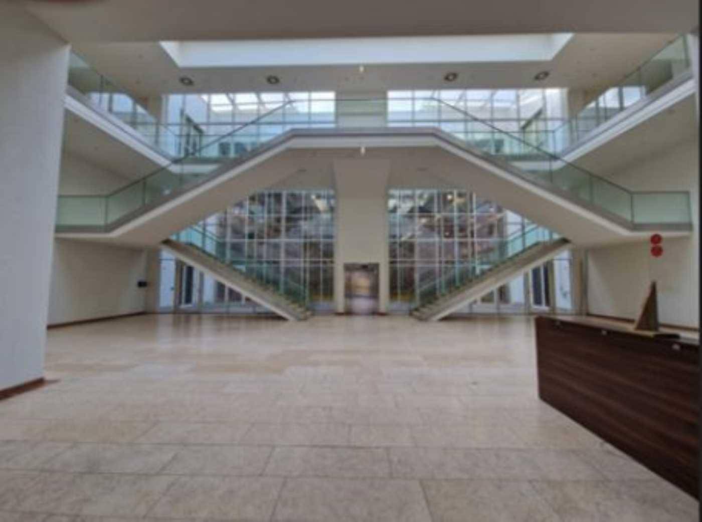 Heller Empfangsbereich mit beeindruckender Doppeltreppe, Glasgeländern und großzügigem Oberlicht.