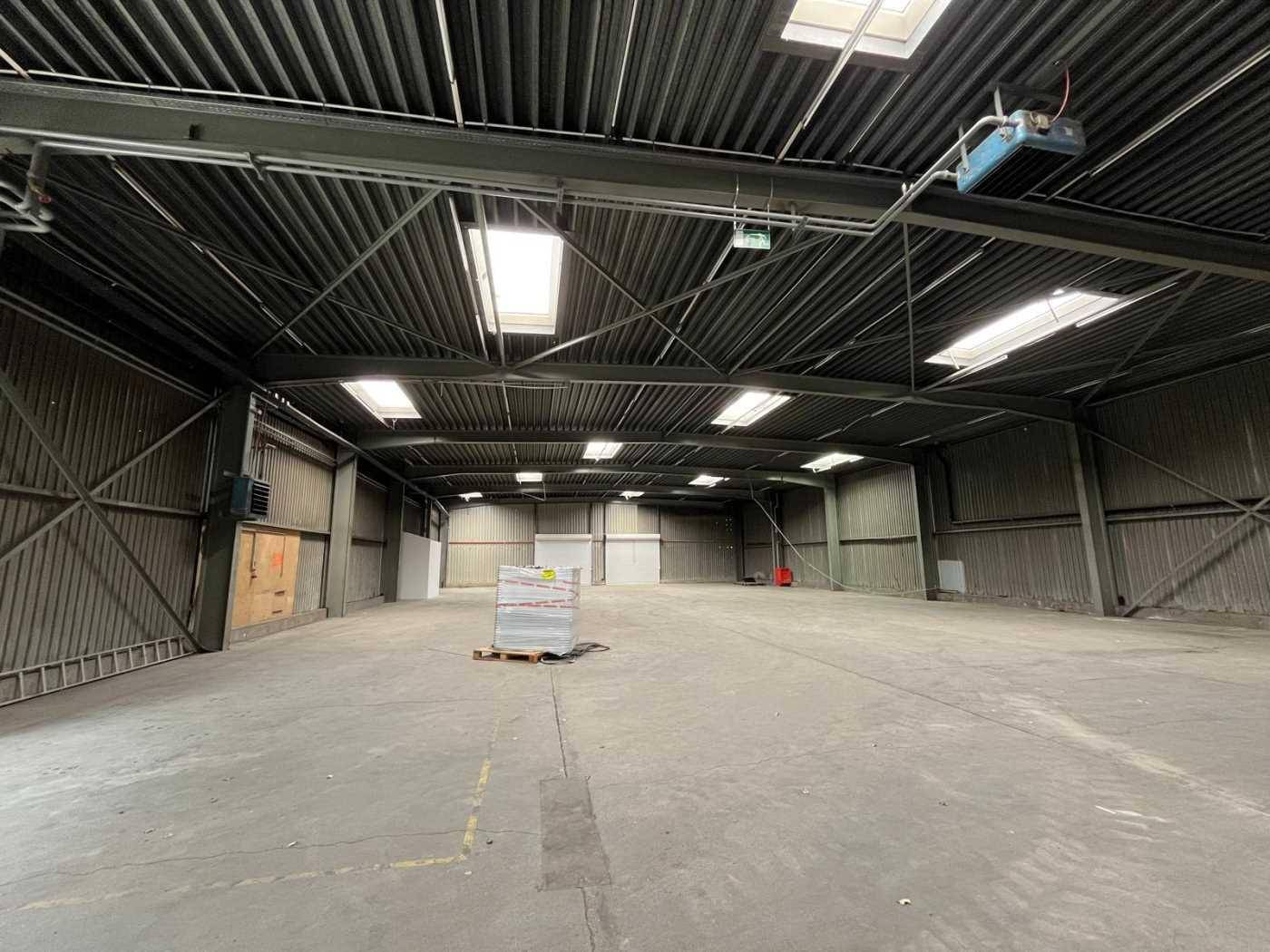 Große, leere Lagerhalle mit hohen Decken, Oberlichtern und einem Betonboden, bereit zur Nutzung.
