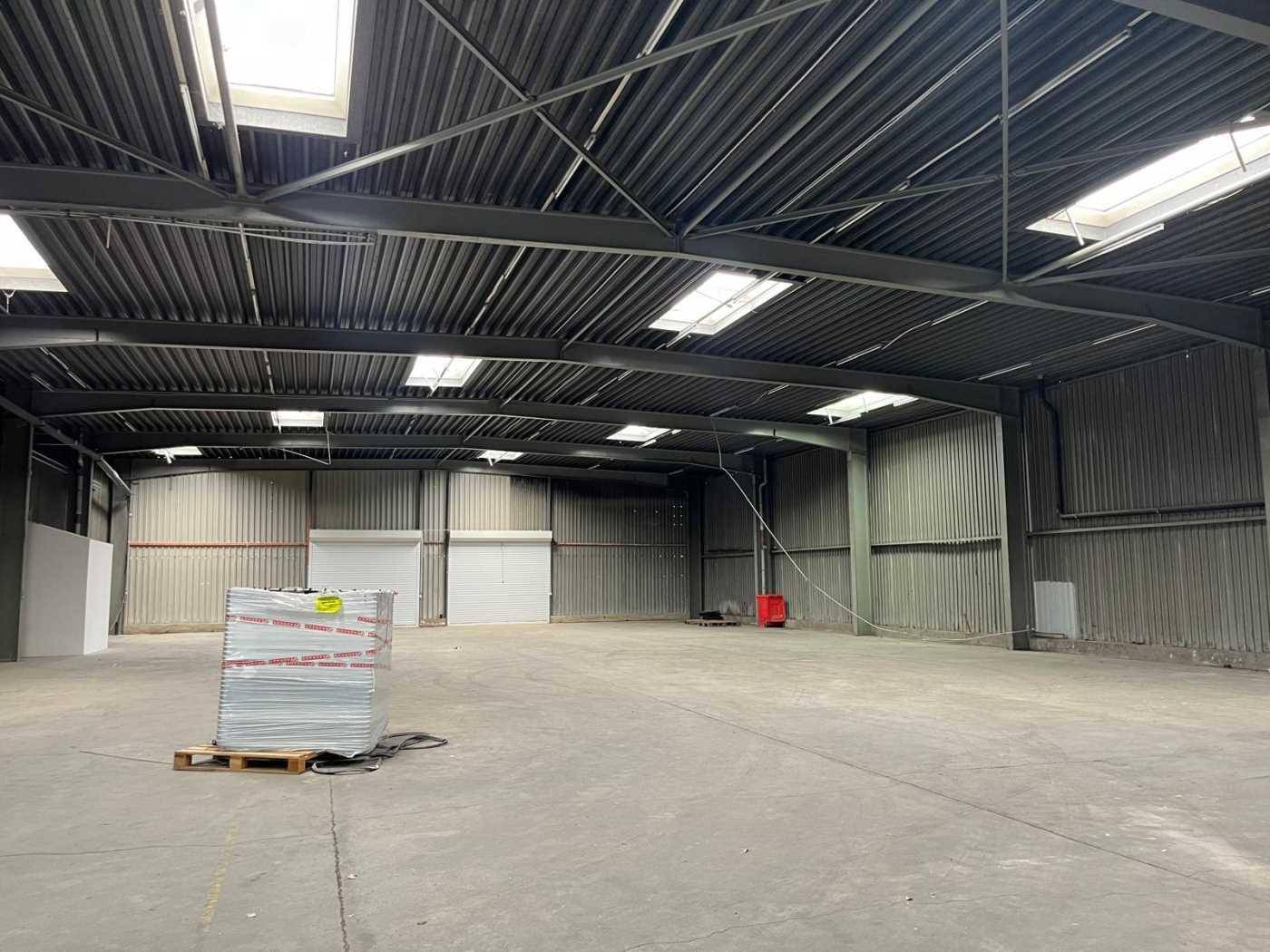 Geräumige Lagerhalle mit hohen Decken, Oberlichtern und einem Betonboden, ideal für Logistik und Lagerung.
