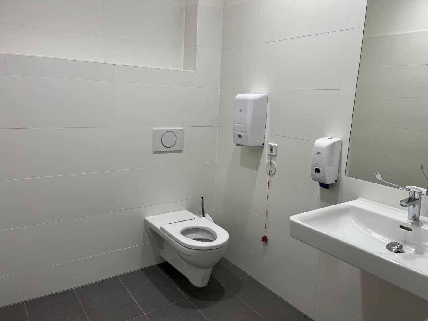 Modernes Badezimmer mit wandhängender Toilette, Waschbecken und weißen Fliesen an den Wänden und auf dem Boden.