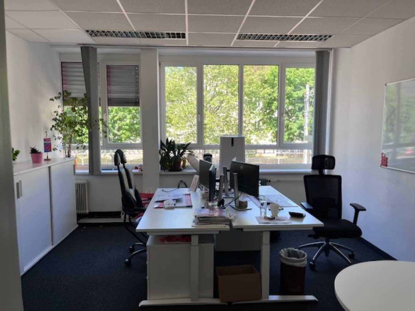 Helles Einzelbüro mit zwei Arbeitsplätzen, großen Fenstern und Blick ins Grüne.