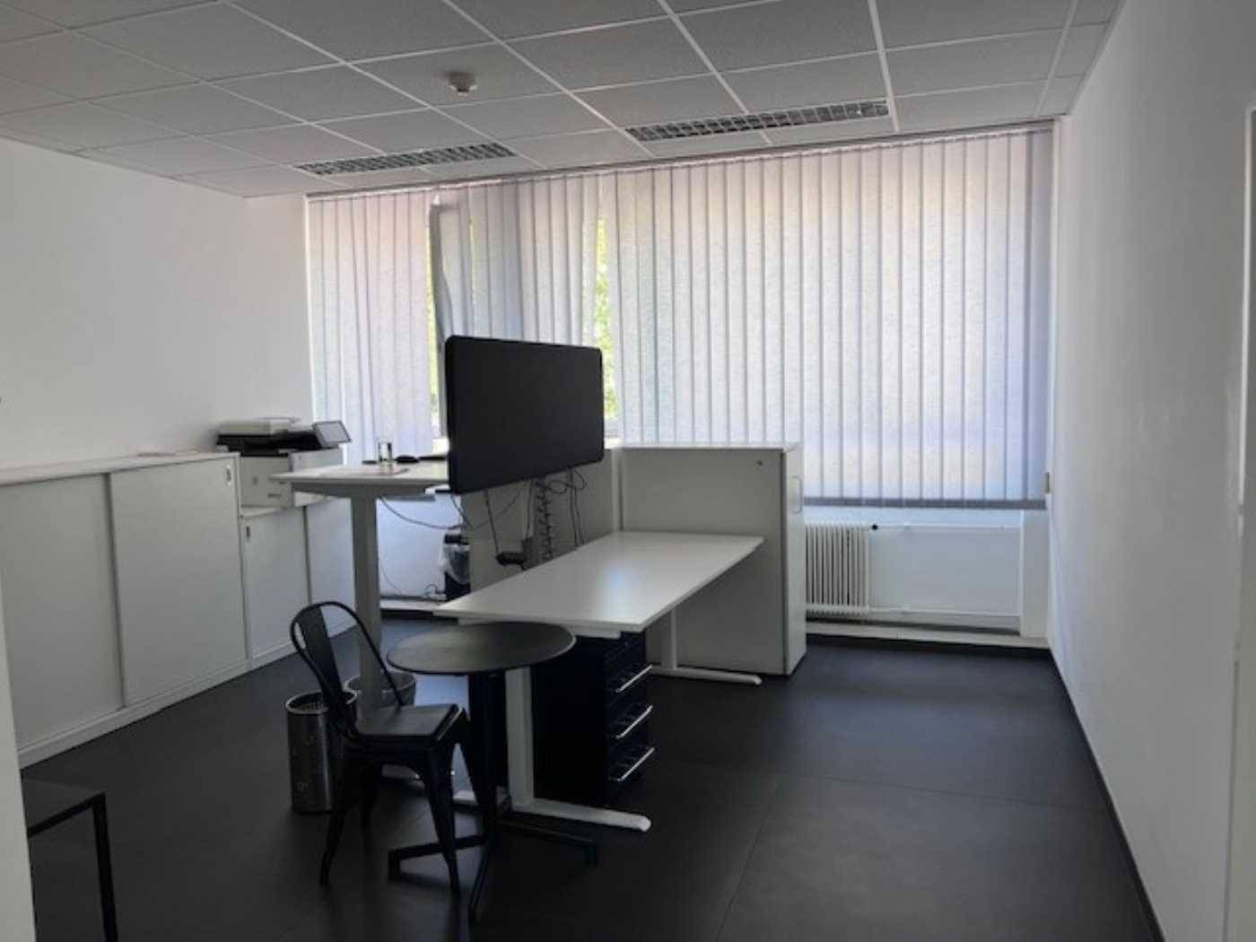 Einzelbüro mit einem Arbeitsplatz, großen Fenstern und vertikalen Jalousien für Privatsphäre.