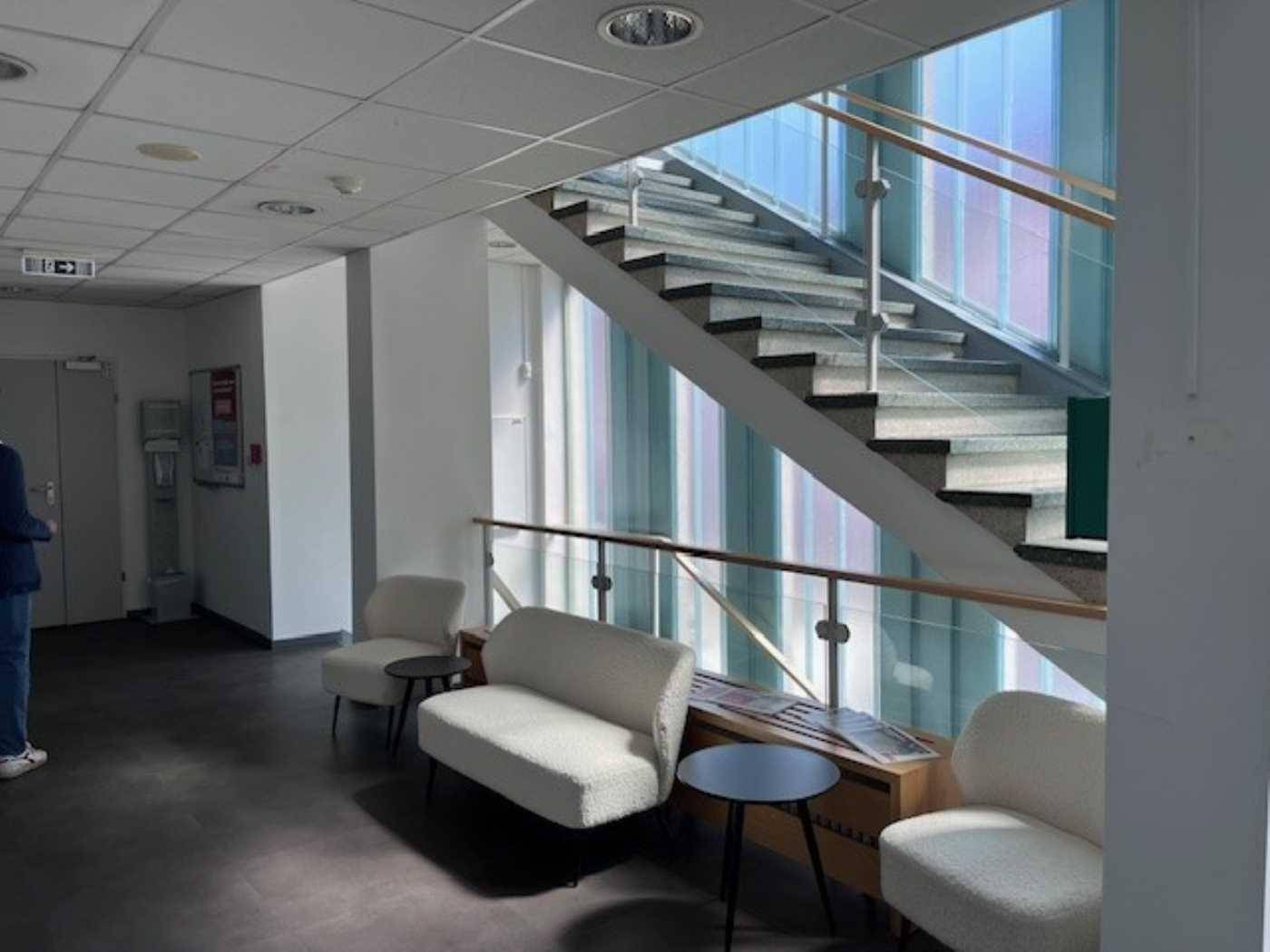 Empfangsbereich mit bequemen Sitzgelegenheiten und einer modernen Treppe mit Glasgeländer.