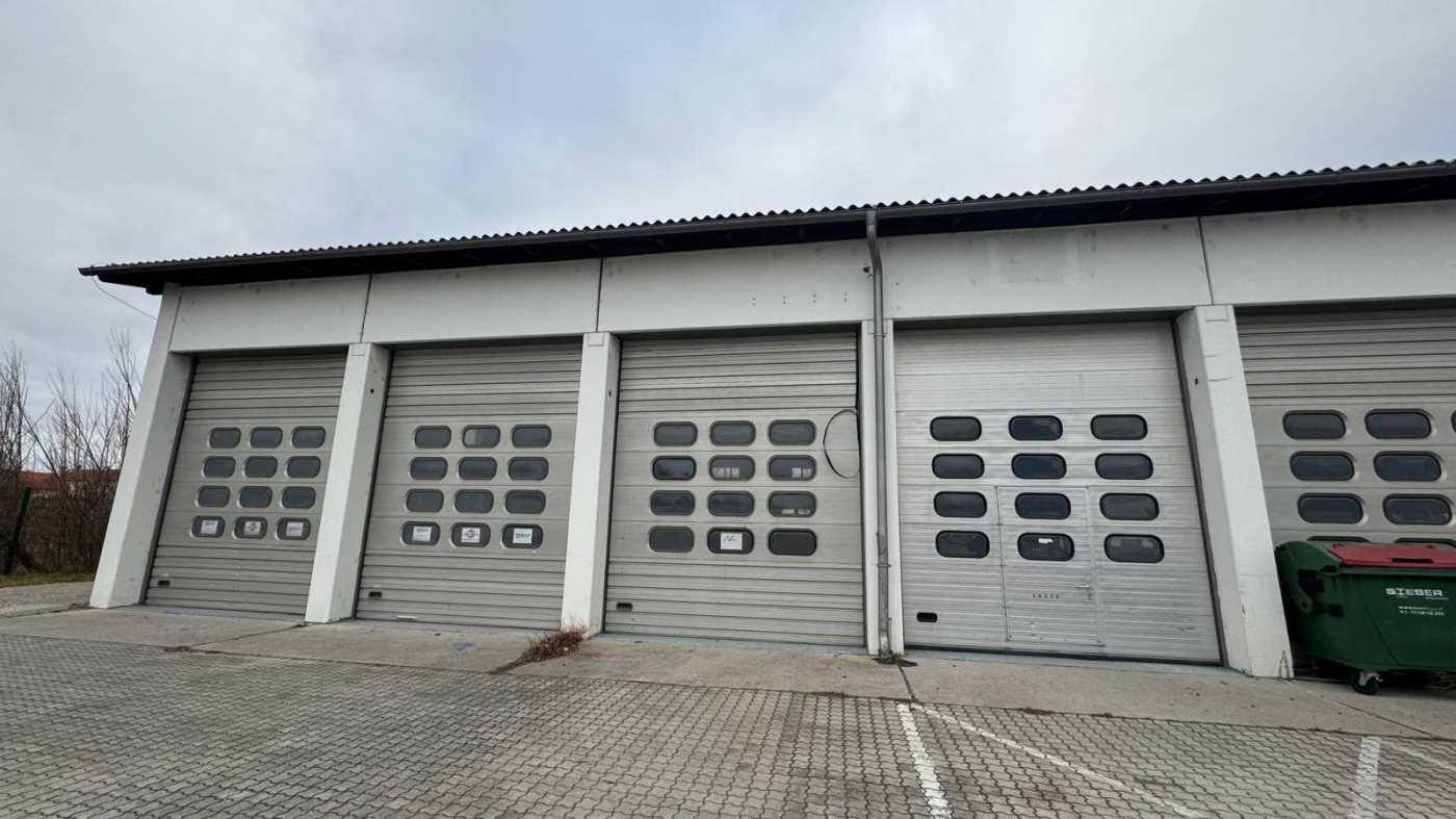 Fassade eines Lagergebäudes mit mehreren Rolltoren und einem Müllcontainer davor.