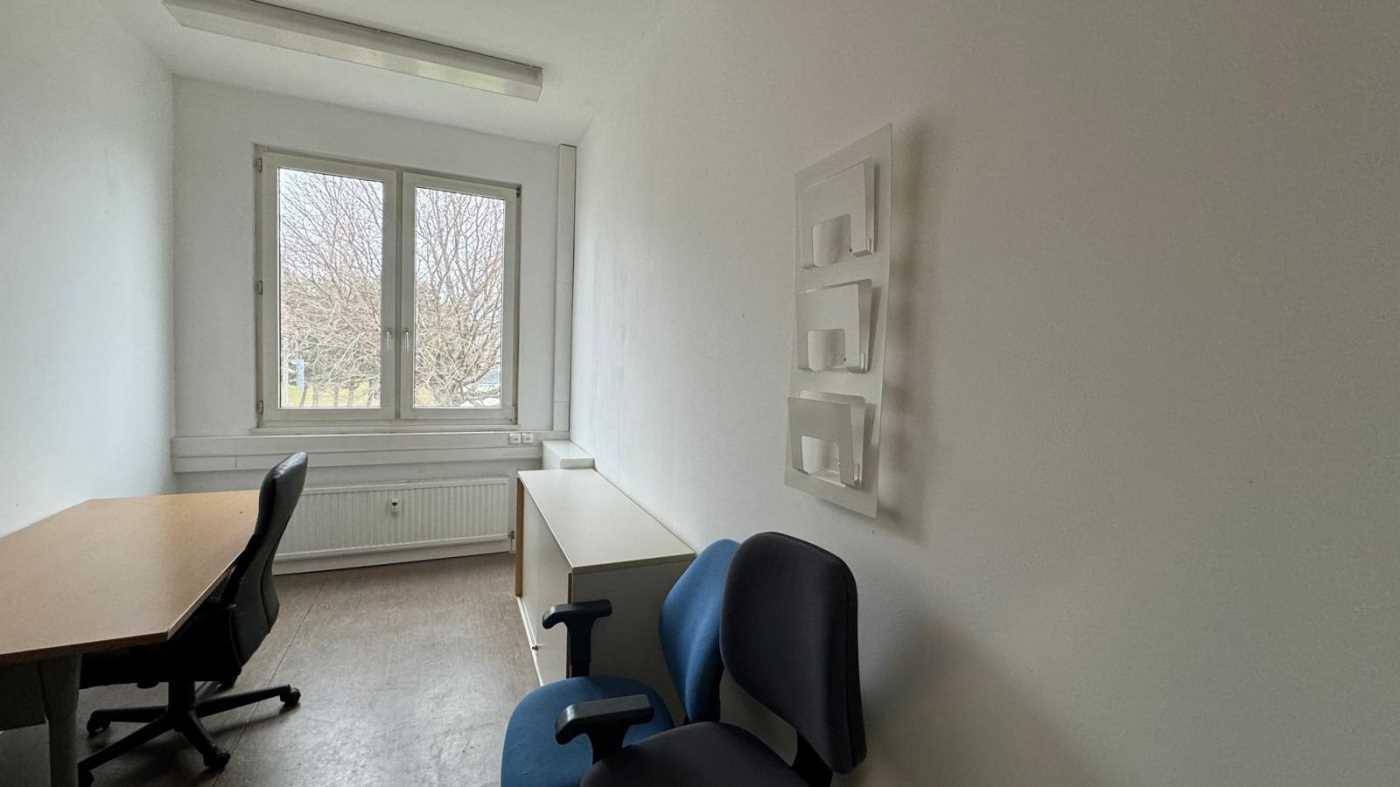Kleines, helles Büro mit einem Schreibtisch, Bürostühlen und einem Fenster.