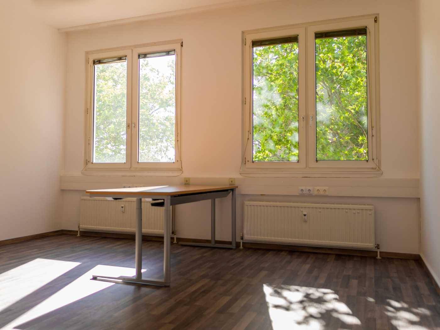 Leeres Büro mit Holzfußboden, großen Fenstern und viel natürlichem Licht.