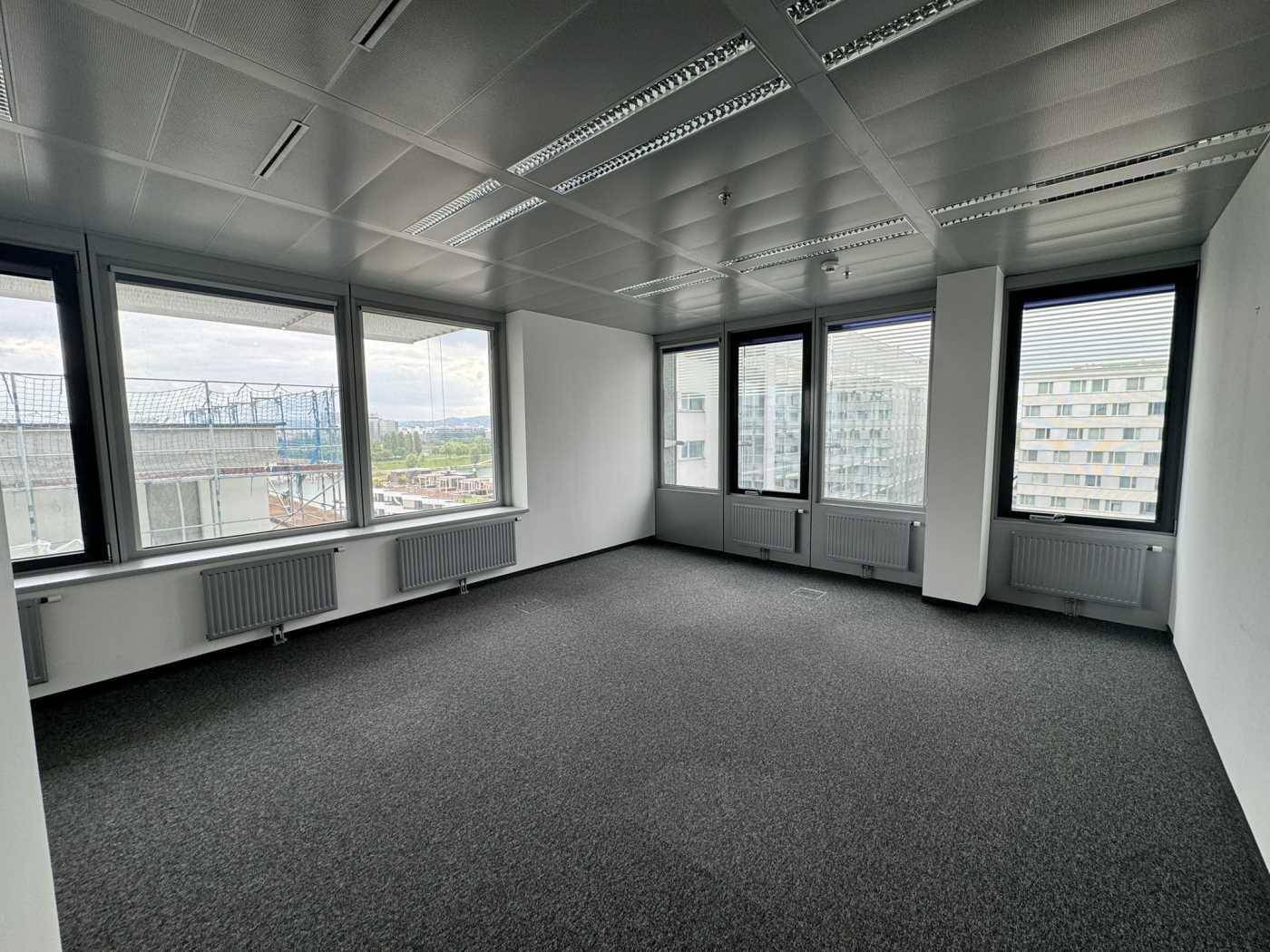 Heller Büroraum mit Teppichboden und Fenstern, die einen weiten Blick über die Stadt bieten und für viel Helligkeit sorgen.