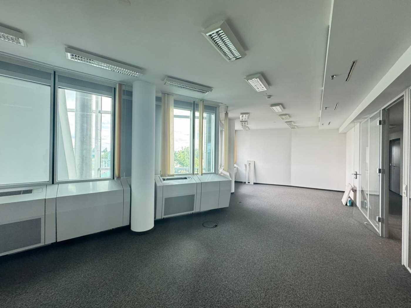 Heller Büroraum mit Teppichboden, großen Fenstern und weißen Wänden.