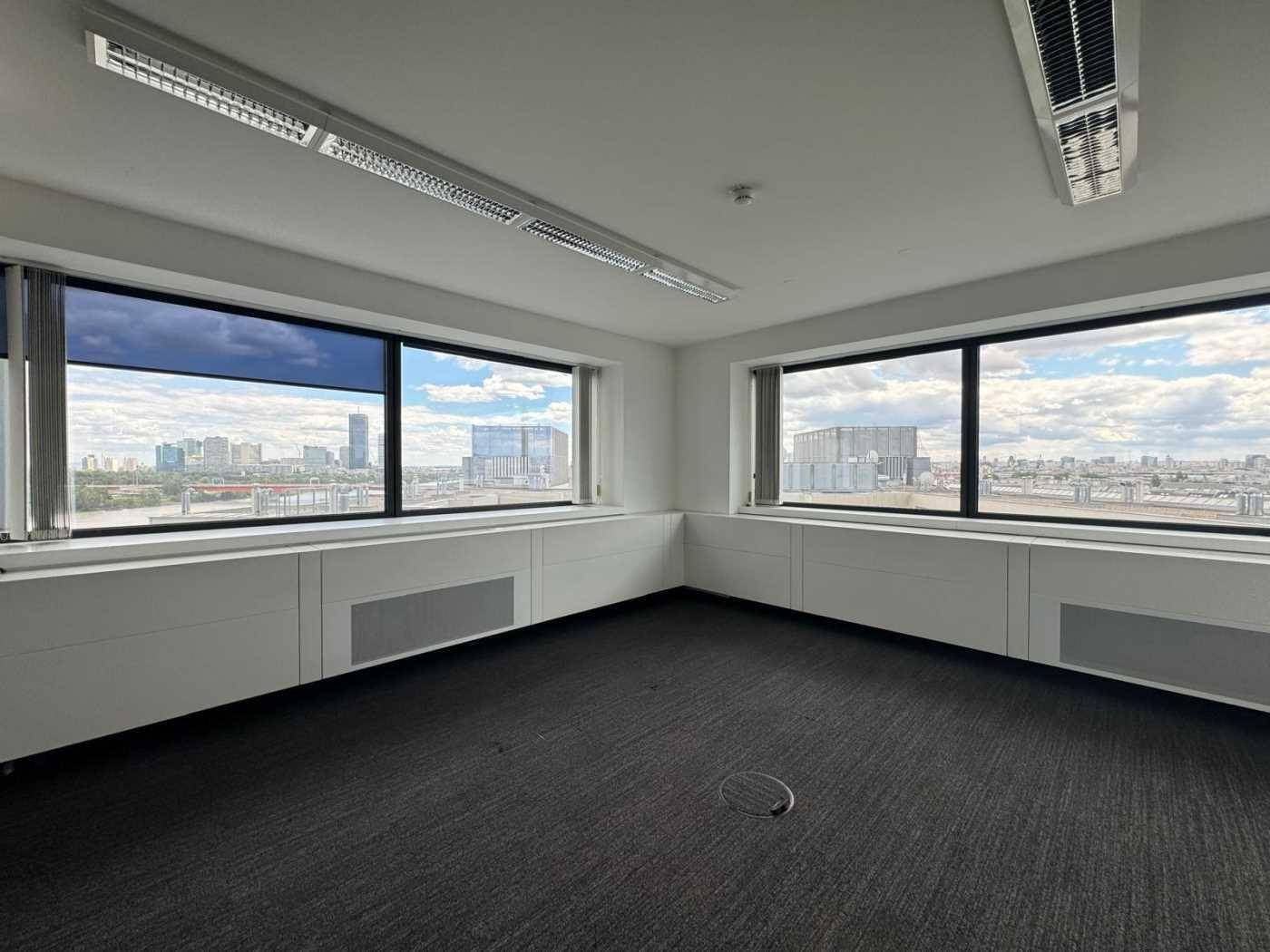 Büroraum mit Teppichboden und großen Fenstern, die einen weiten Blick auf die Stadt bieten.